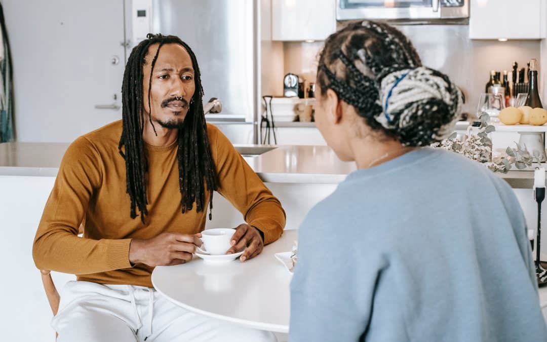 A straight couple at a kitchen table talking about their relationship over a cup of tea. It's serious, but not confrontational